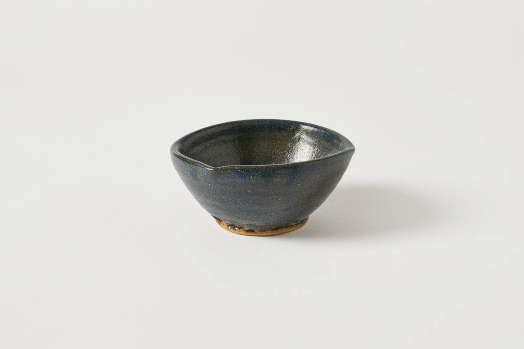 A small handmade ceramic bowl with a dark blue and black glaze, featuring a rustic brown clay base, photographed on a clean white background.